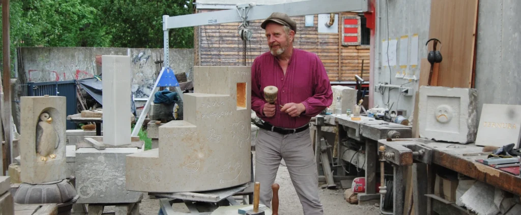 Michael Spengler arbeitet in seiner Werkstatt an einem Grabmal und blickt in die Kamera
